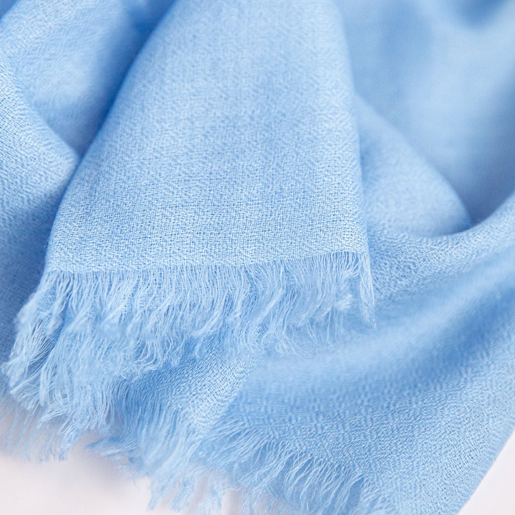 Close-up of a light blue scarf with frayed edges on a white background